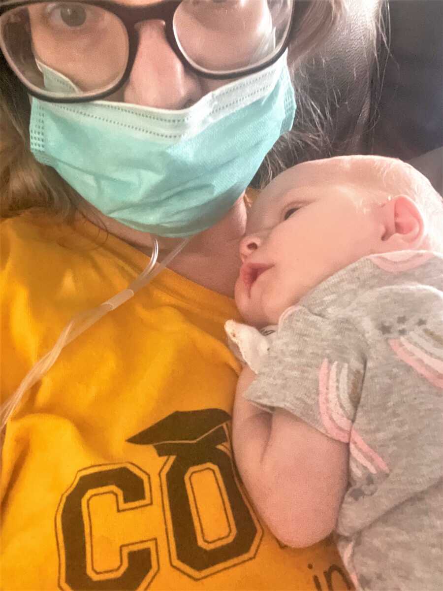 new mom battling COVID holding newborn baby in her chest and wearing a mask