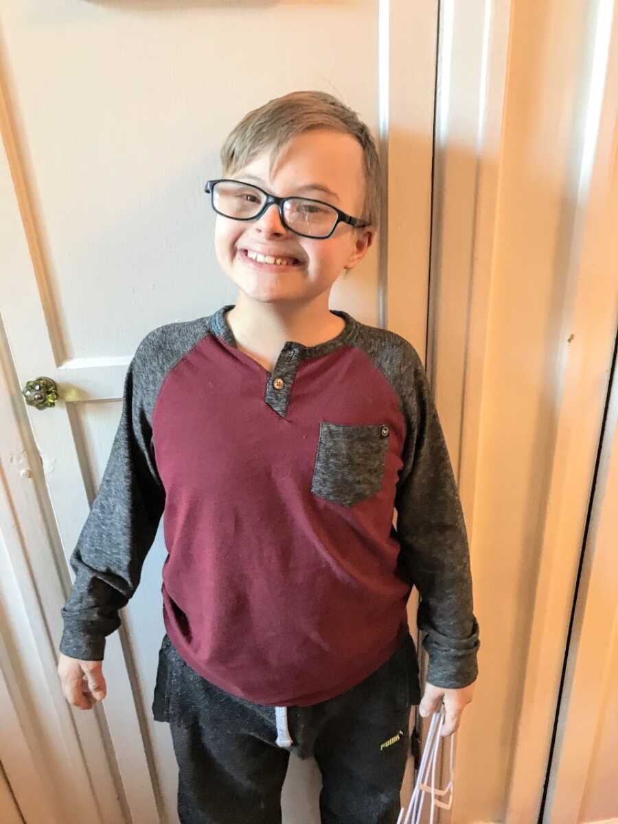 Little boy with Down syndrome smiles big for the camera in long-sleeved shirt and sweats