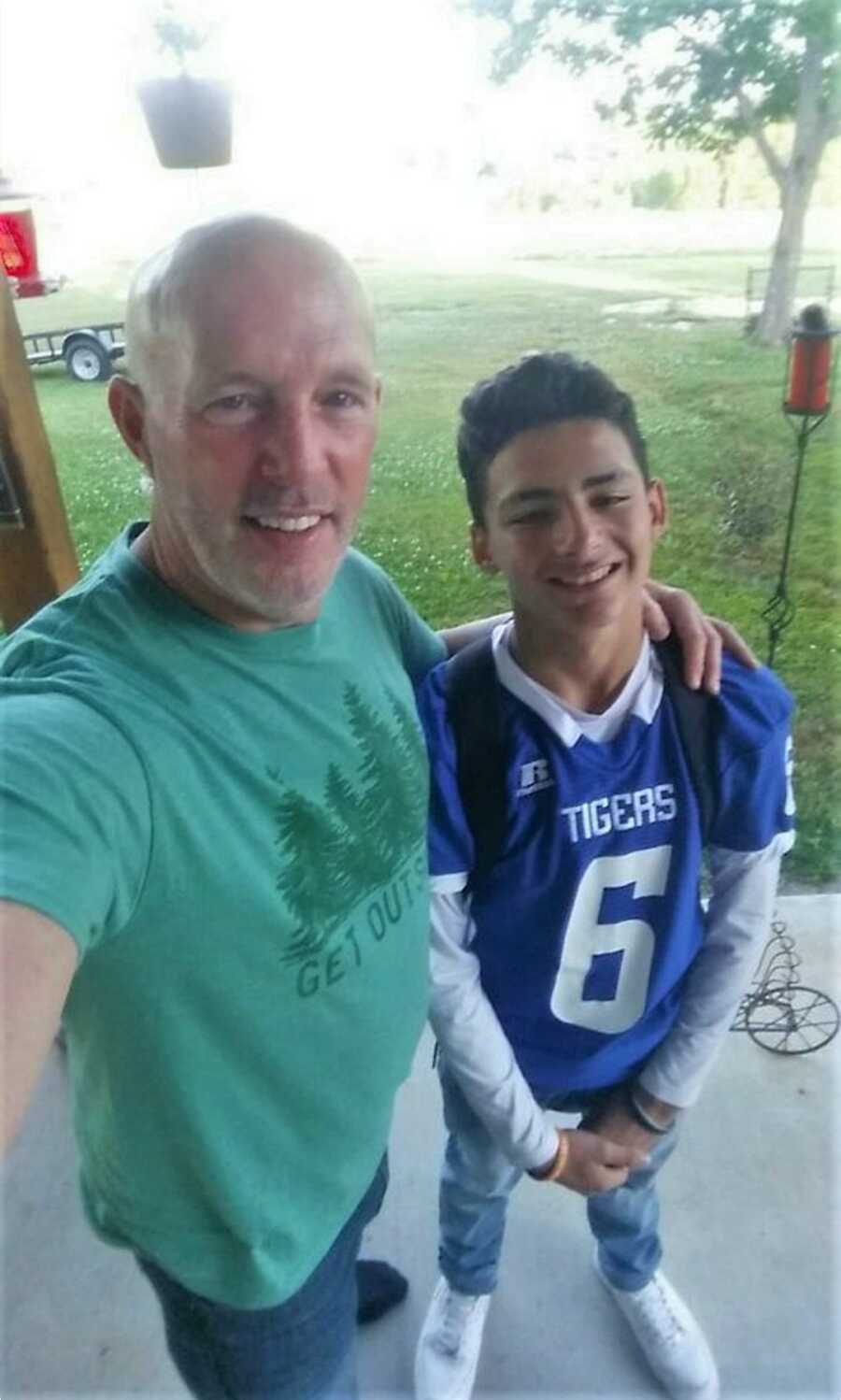 Single dad and adoptive son get ready for school wearing a Tigers shirt in color purple and a green shirt with trees and the words get outside 