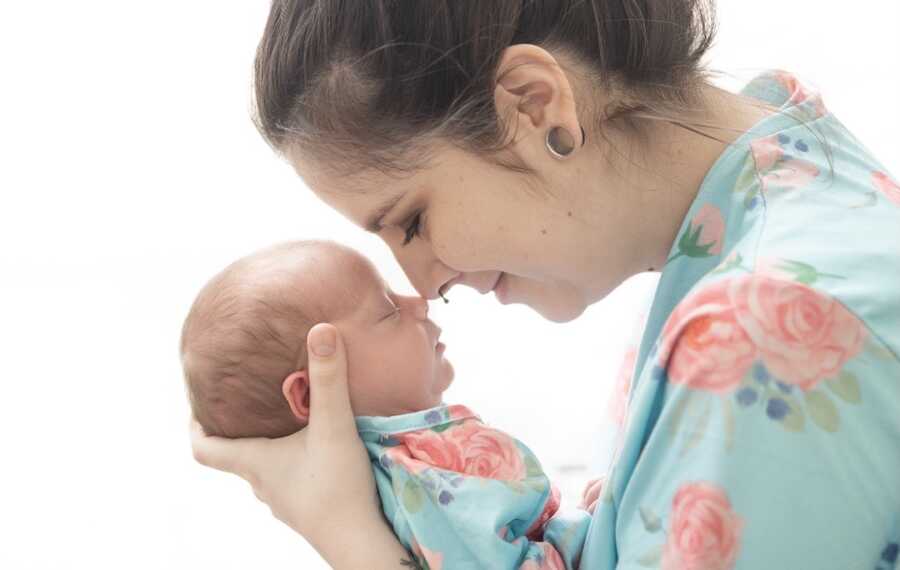 side profile of mother holding baby girl close to her face touching noses 