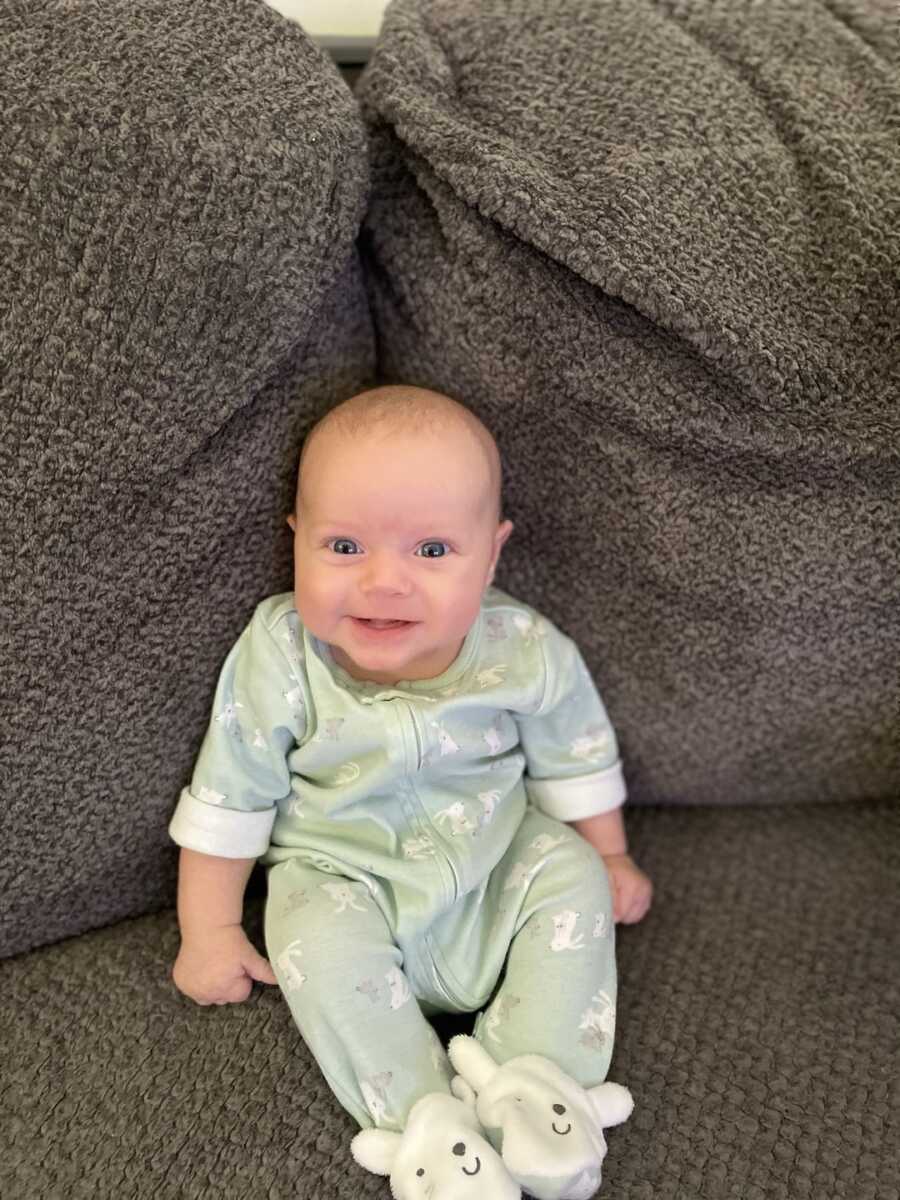 baby girl sitting on couch between two cushions wearing a onesie 