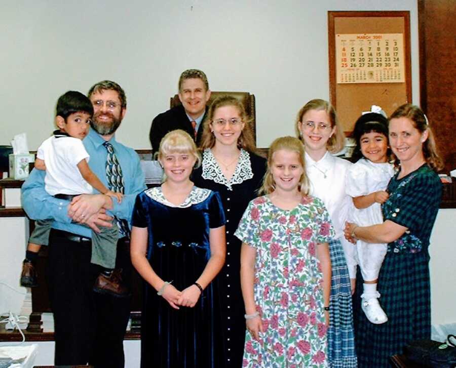Large family with four biological daughters smile for a photo with two little siblings they just officially adopted in a courtroom