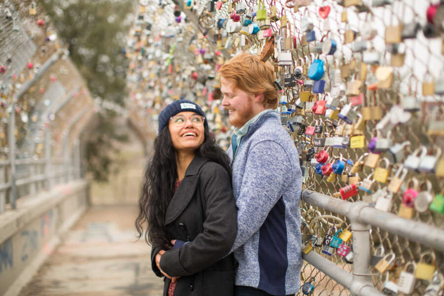 Couple share intimate moment during engagement photoshoot on bridge covered in locks