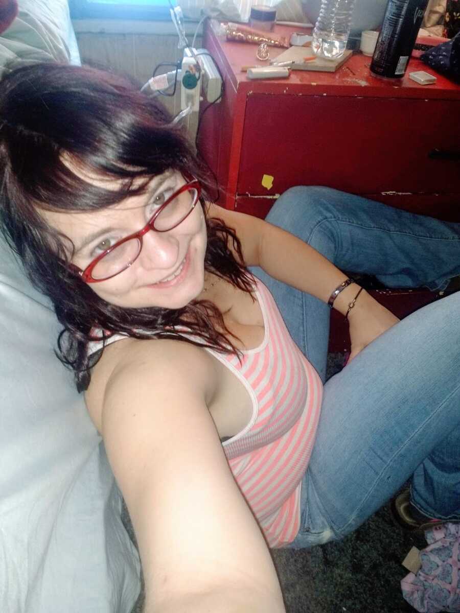 A former drug addict sits on the floor wearing glasses