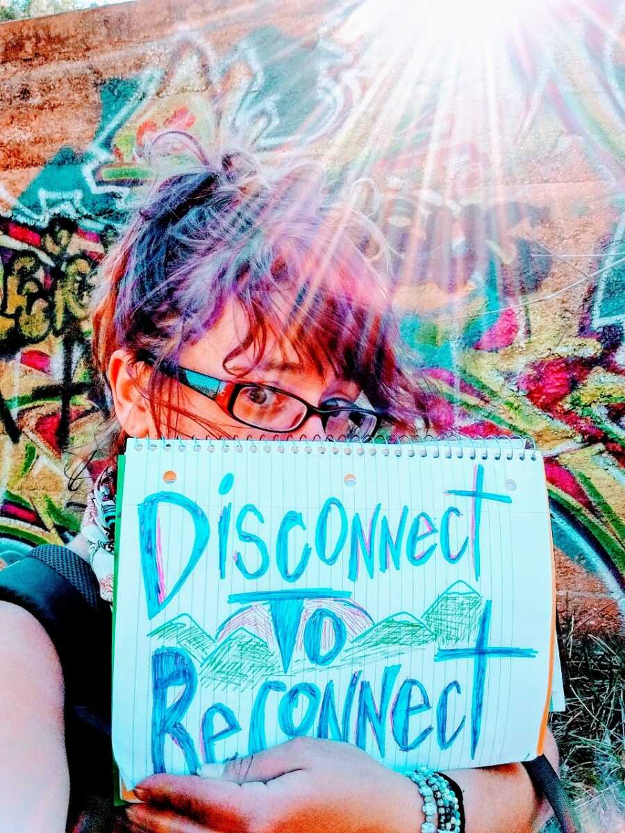 A mom holds up a sign saying "Disconnect to Reconnect"