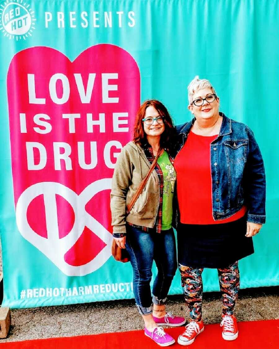 A recovering addict and another woman pose in front of a sign