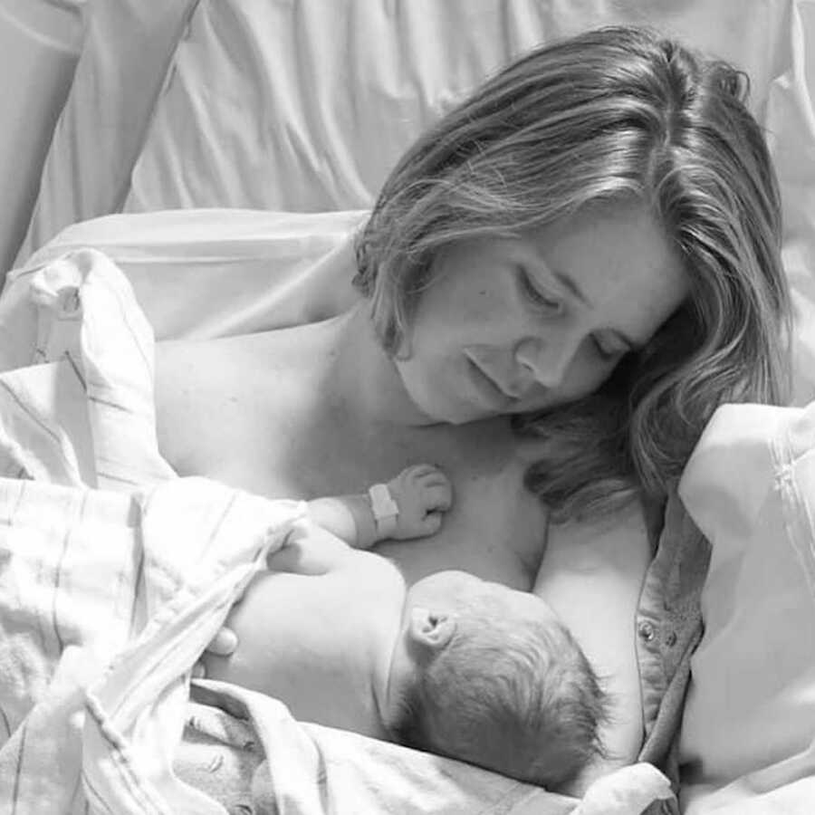 mother holds her newborn child on her bare chest and looks at them adoringly