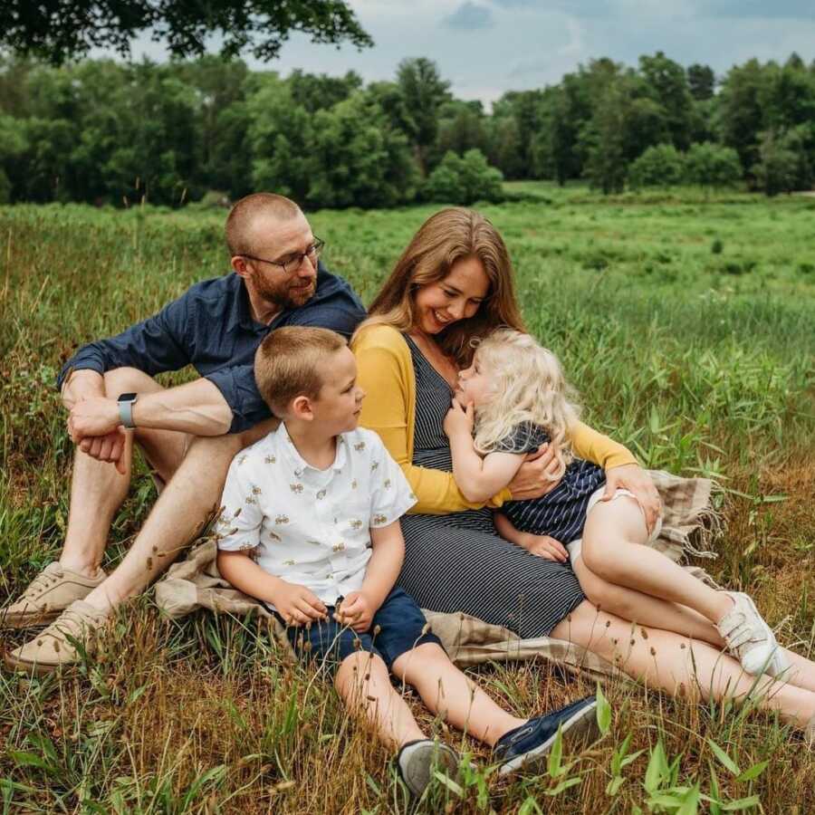 mother and father sitting in field with their two children, a daughter and son