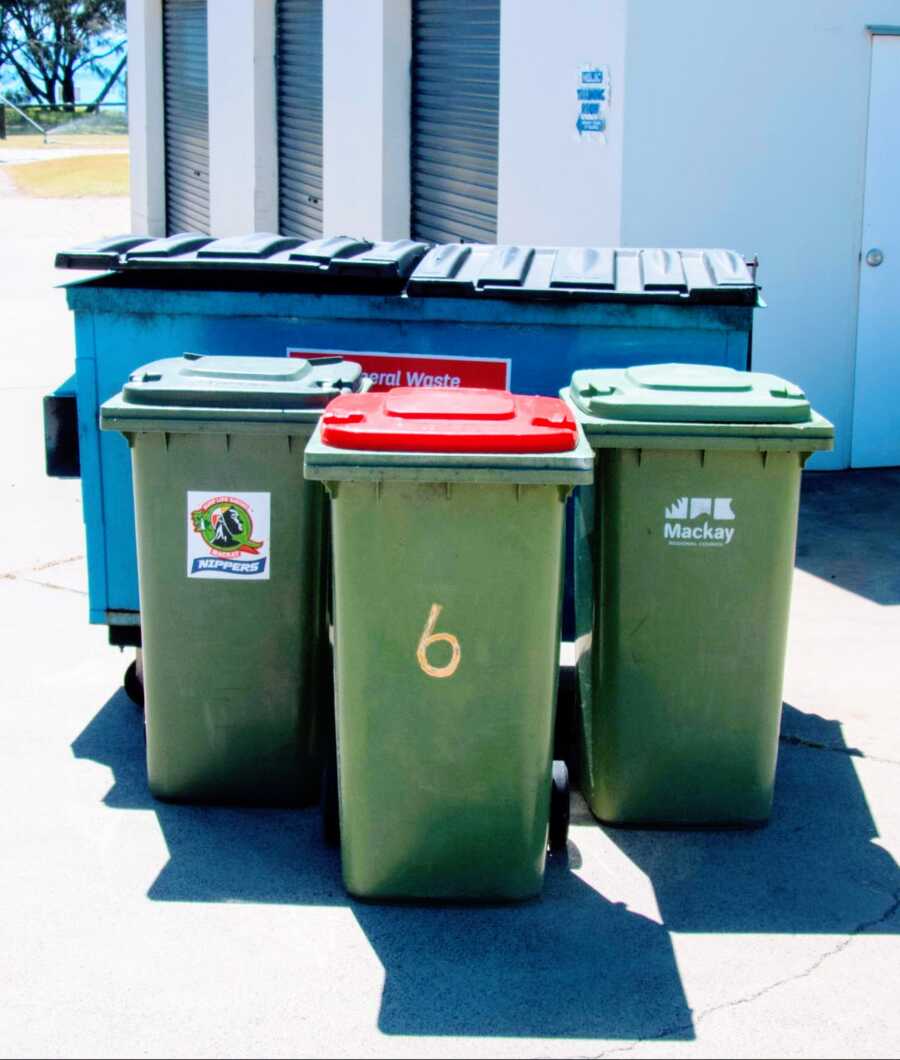 three garbage cans placed in front of a dumpster