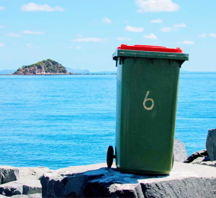 garbage can is placed in front of a scenic view of the water with an island in the distance