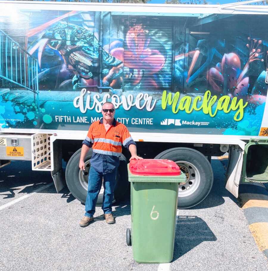man poses with garbage can in front of a "discover mackay" truck