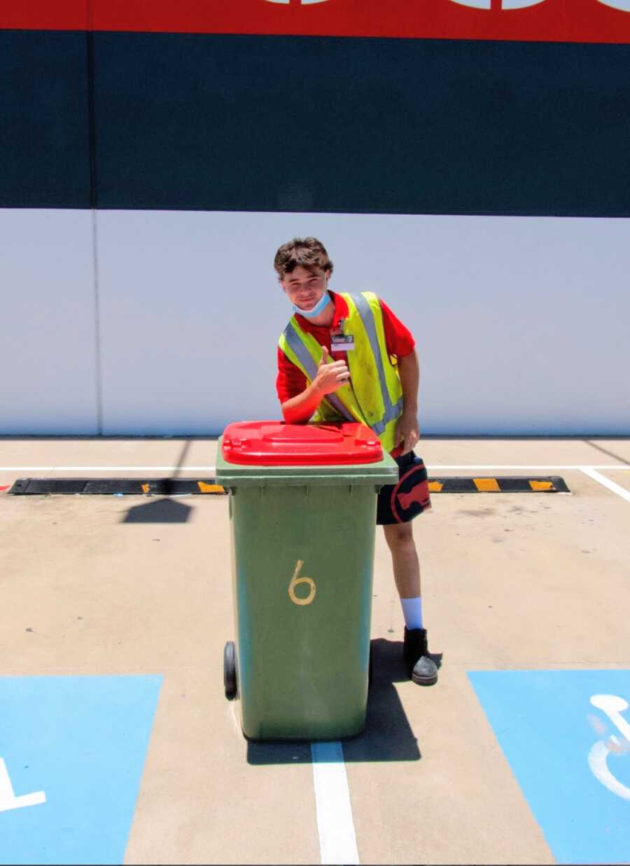 youthful boy poses with garbage can and gives a thumbs up