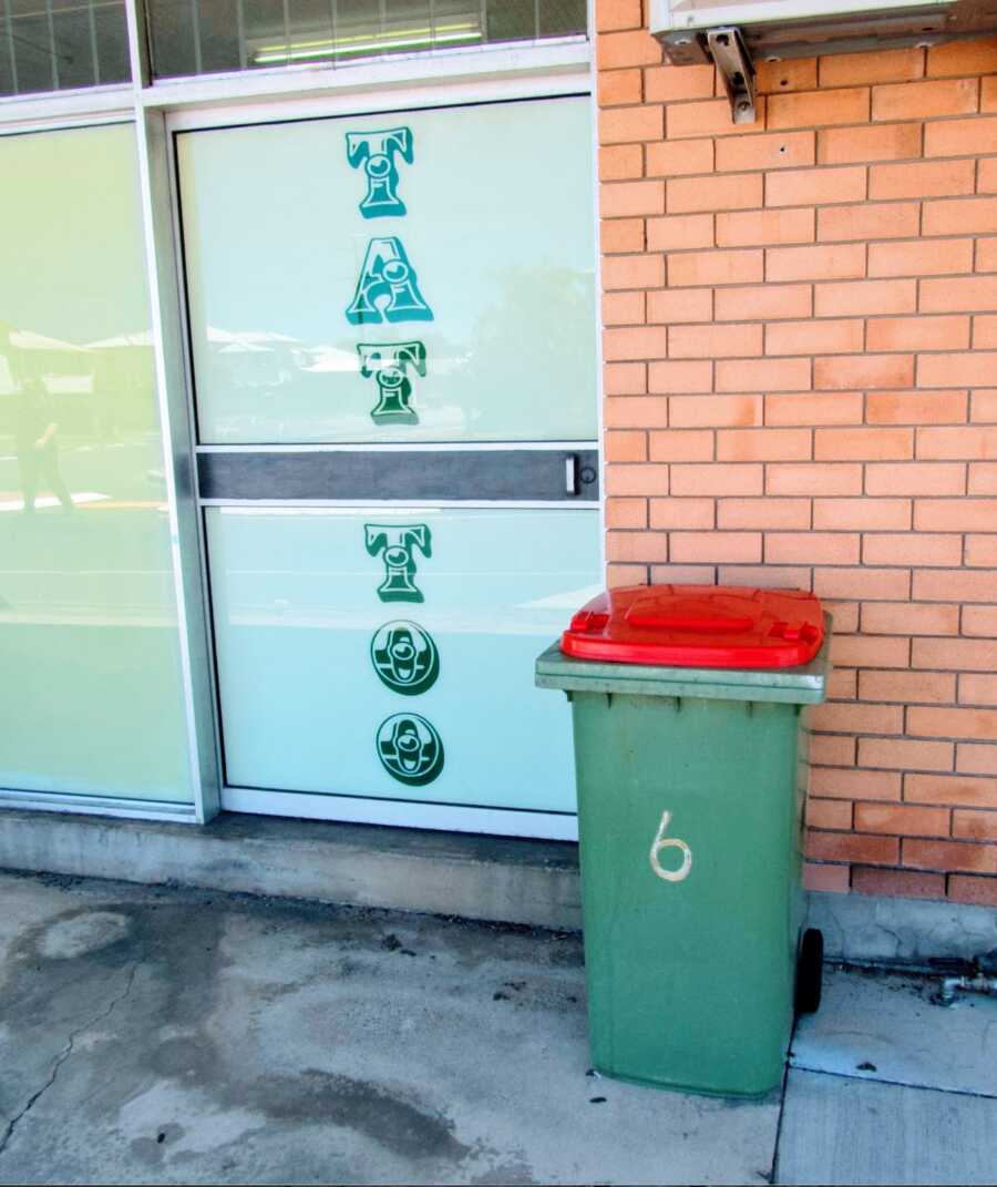 person brings their neighbor's garbage can out to a tattoo shop