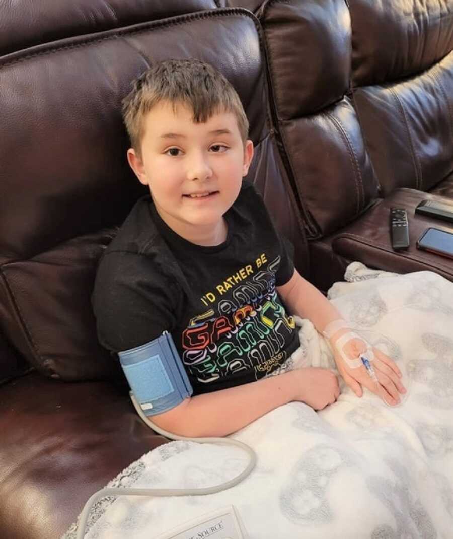 Young boy with Duchenne Muscular Dystrophy sits on couch with IV in his arm.