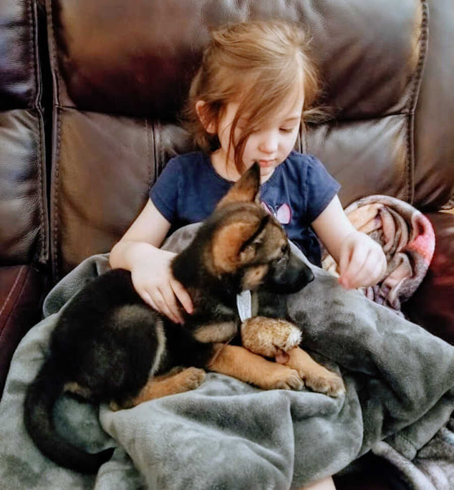 daughter sits on chair with a blanket in her lap and a puppy on top of the blanket