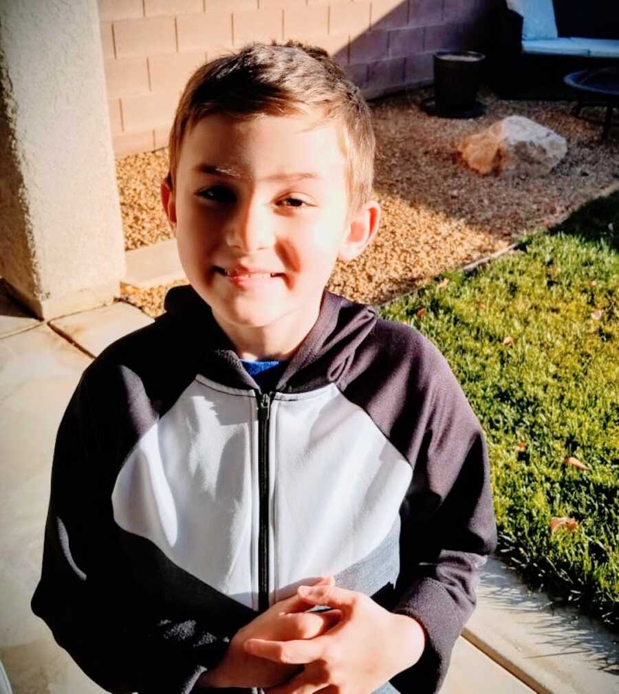 young boy with Duchenne's poses in front of camera with hands together, smiling. 