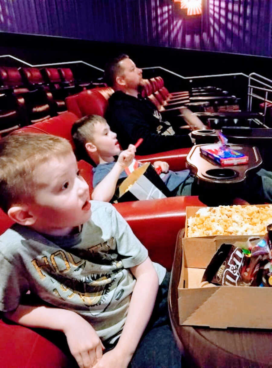 two young boys with Duchenne's sit at the movie theater with their dad