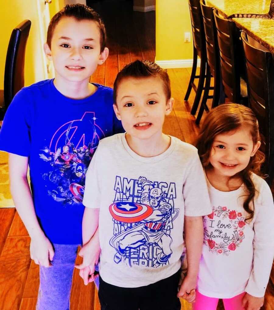 two young boys with Duchenne's stand with their sister and smile towards the camera