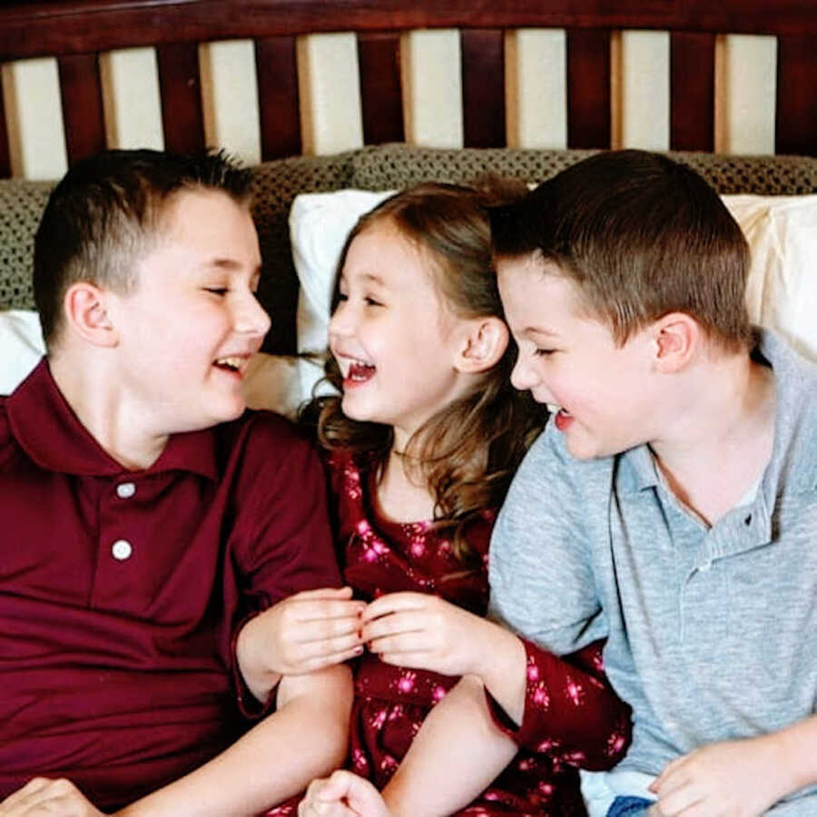 two boys with Duchenne's sit on both sides of their sister, the three children are laughing