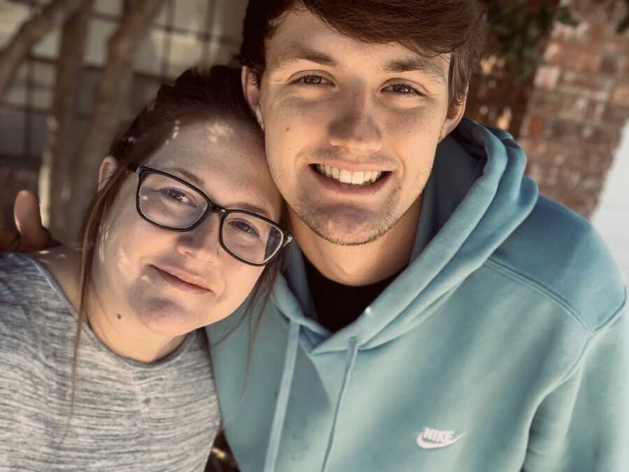 teenage son and mother take a selfie together, son has his head resting on top of his mother's