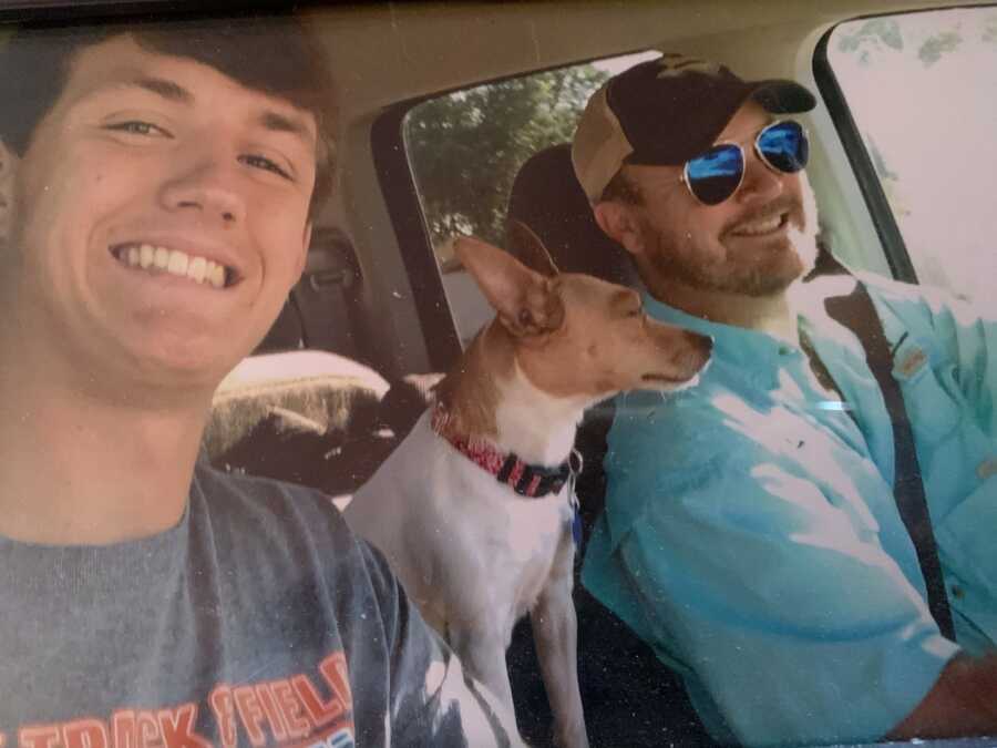 teenage son takes a selfie in the car with his dog and father in the driver seat