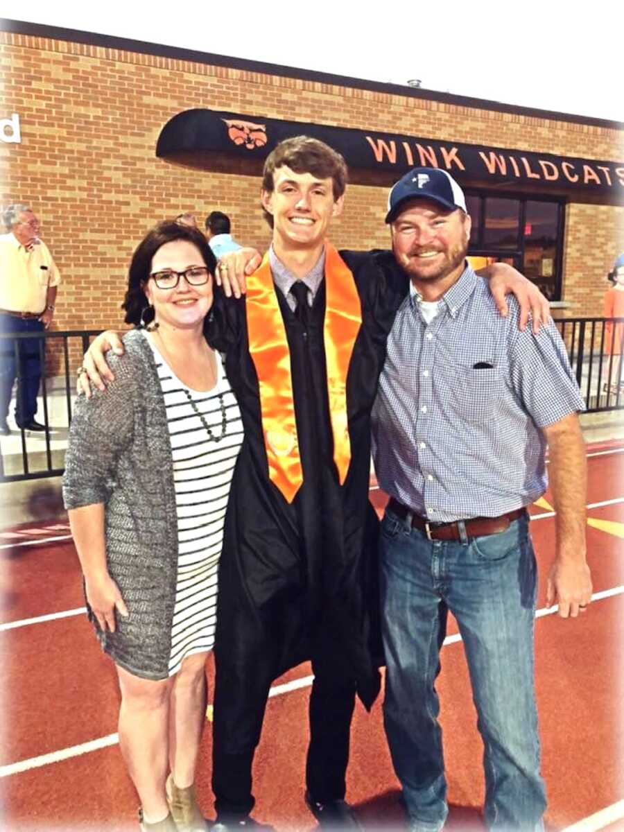 teenage son posed with his mom and dad at his high school graduation, dressed in his gown