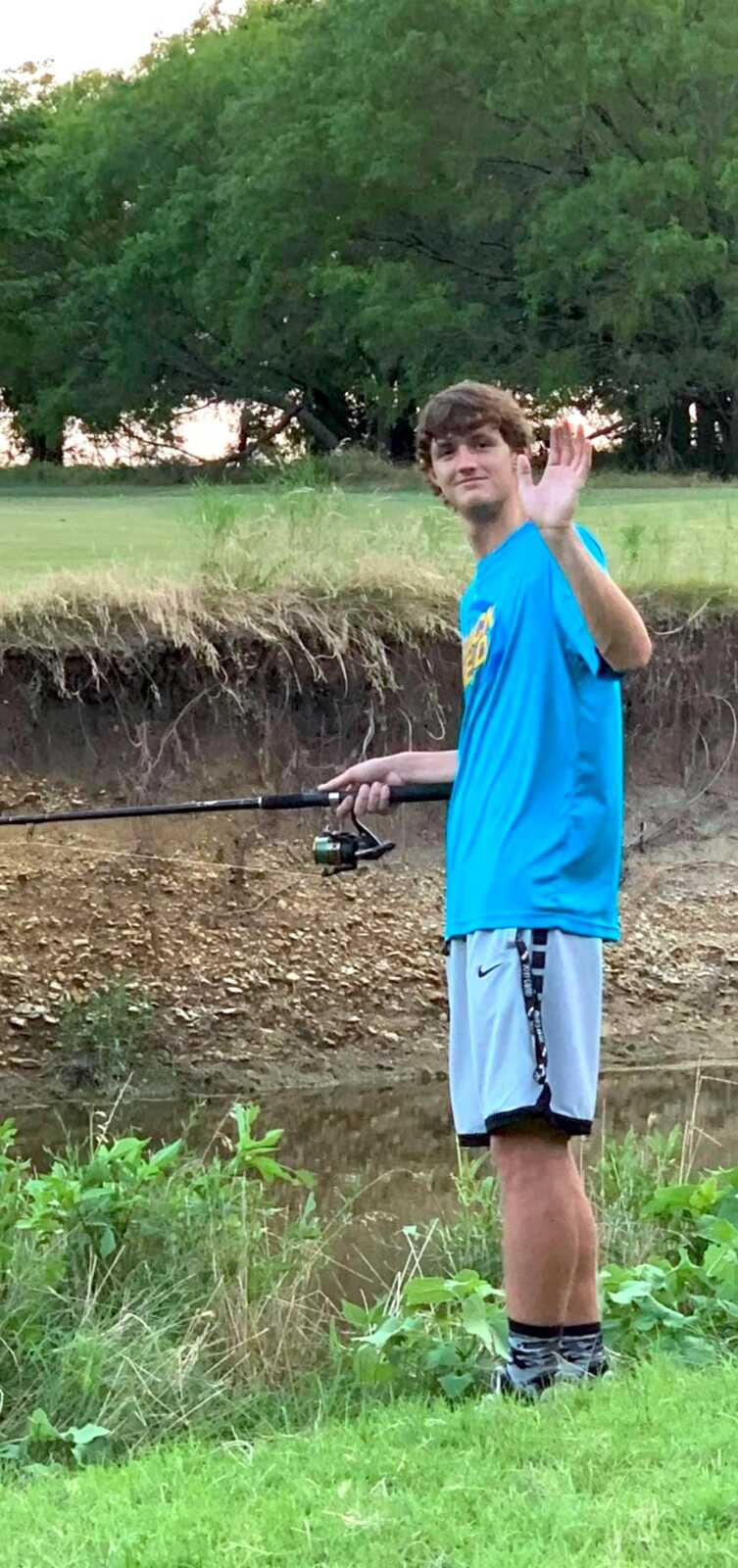 teenage son holds fishing pole while waving at camera