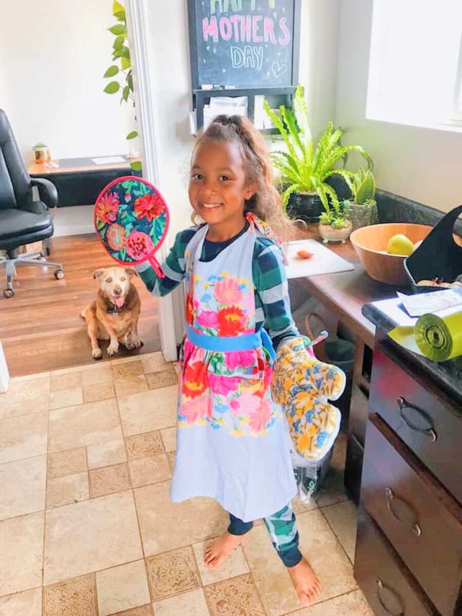 young girl wears apron and oven mitts on Mother's Day