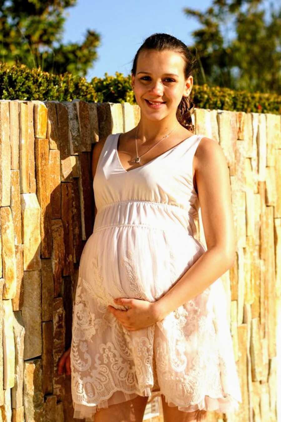 pregnant teen mom poses in a dress smiling while holding her baby bump