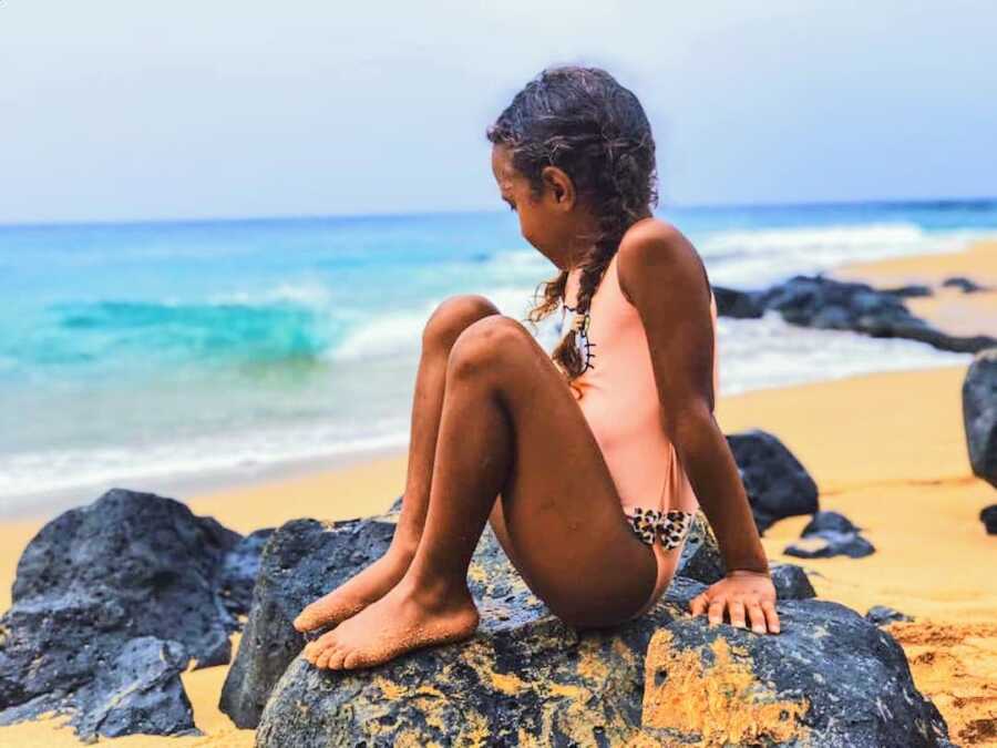 young girl sits on rock at the beach