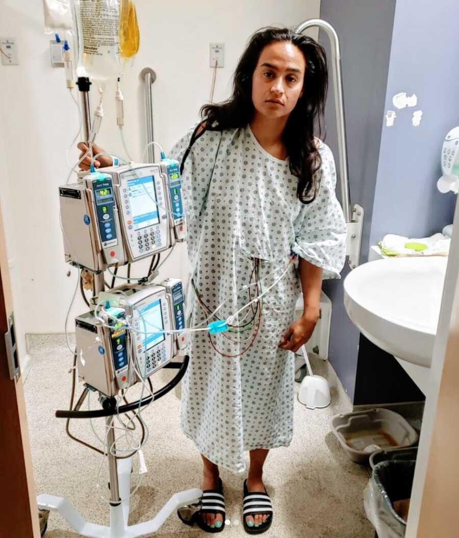 A woman stands in a hospital gown and flipflops