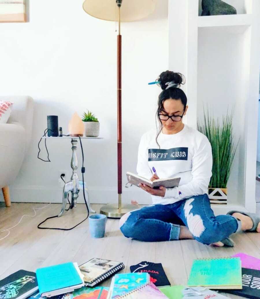 A woman sits on the floor writing in journals