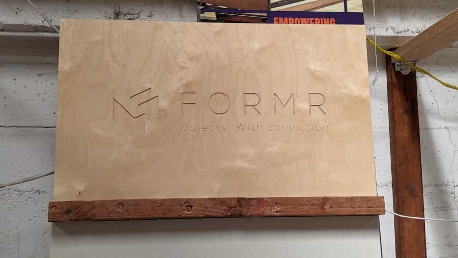 wooden sign engraved with the logo of The Formr along with their slogan