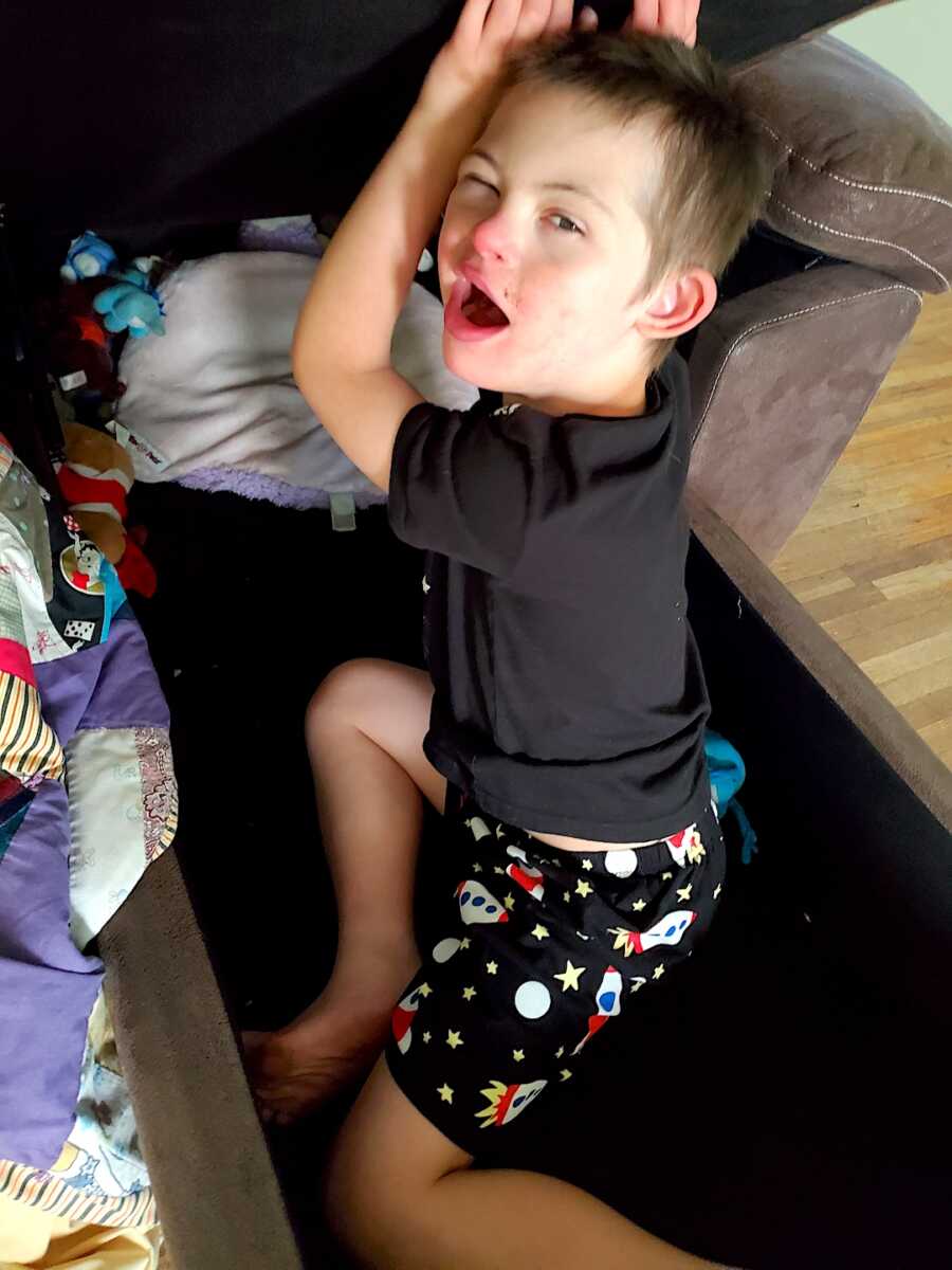 son with down syndrome sits in blanket storage container in pajamas