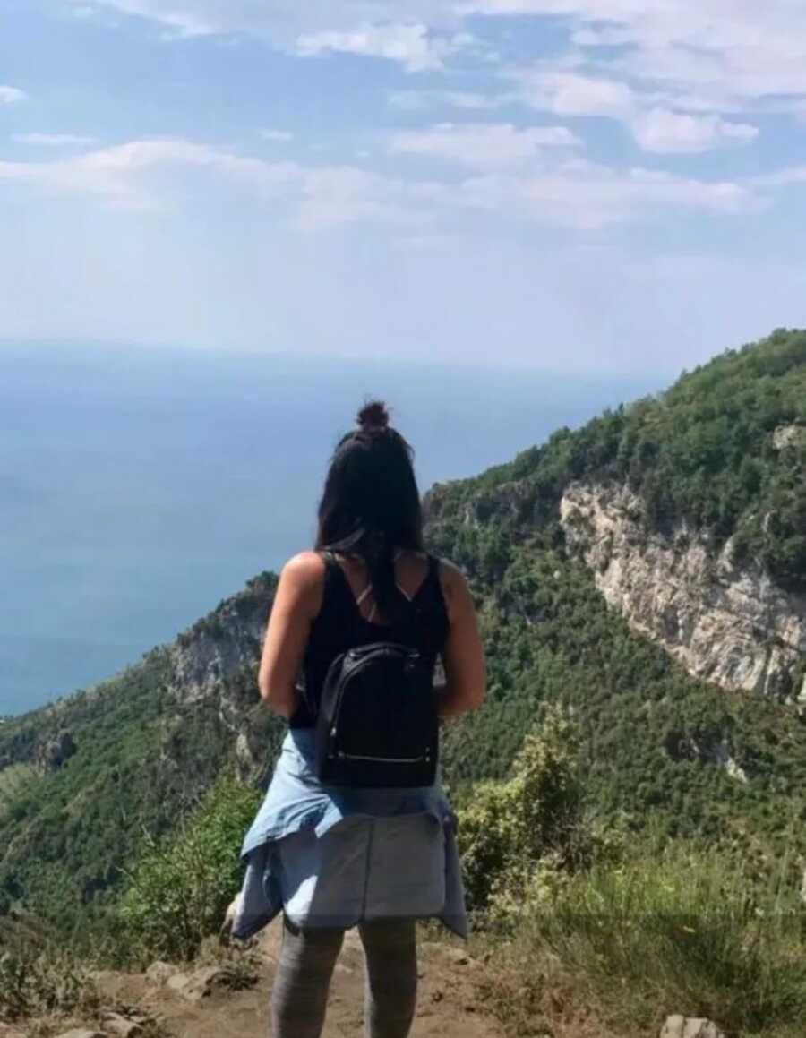 woman standing on top of a rock looking at the ocean