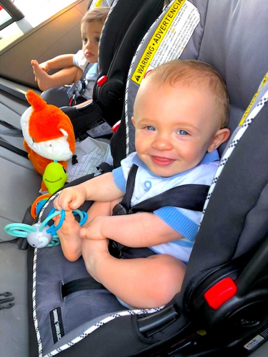 One of two twin boys in his car seat looking at the camera and smiling
