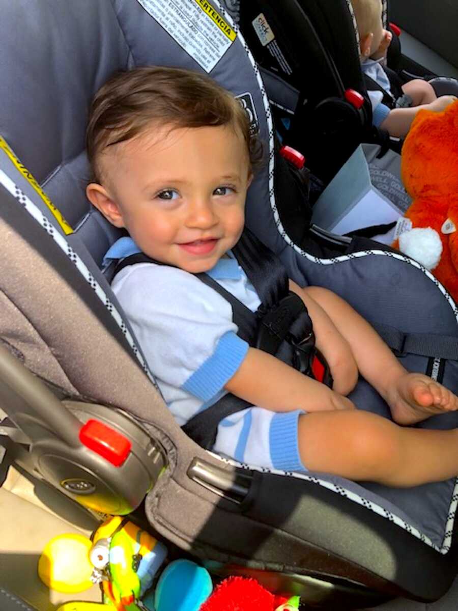 one of two twin boys buckled into their car seat and smiling towards the camera