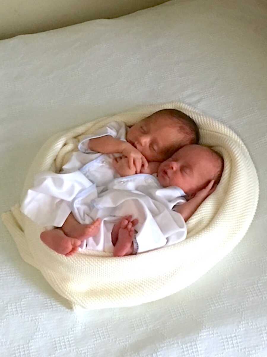 infant twin boys cuddled close to one another and wrapped in blankets