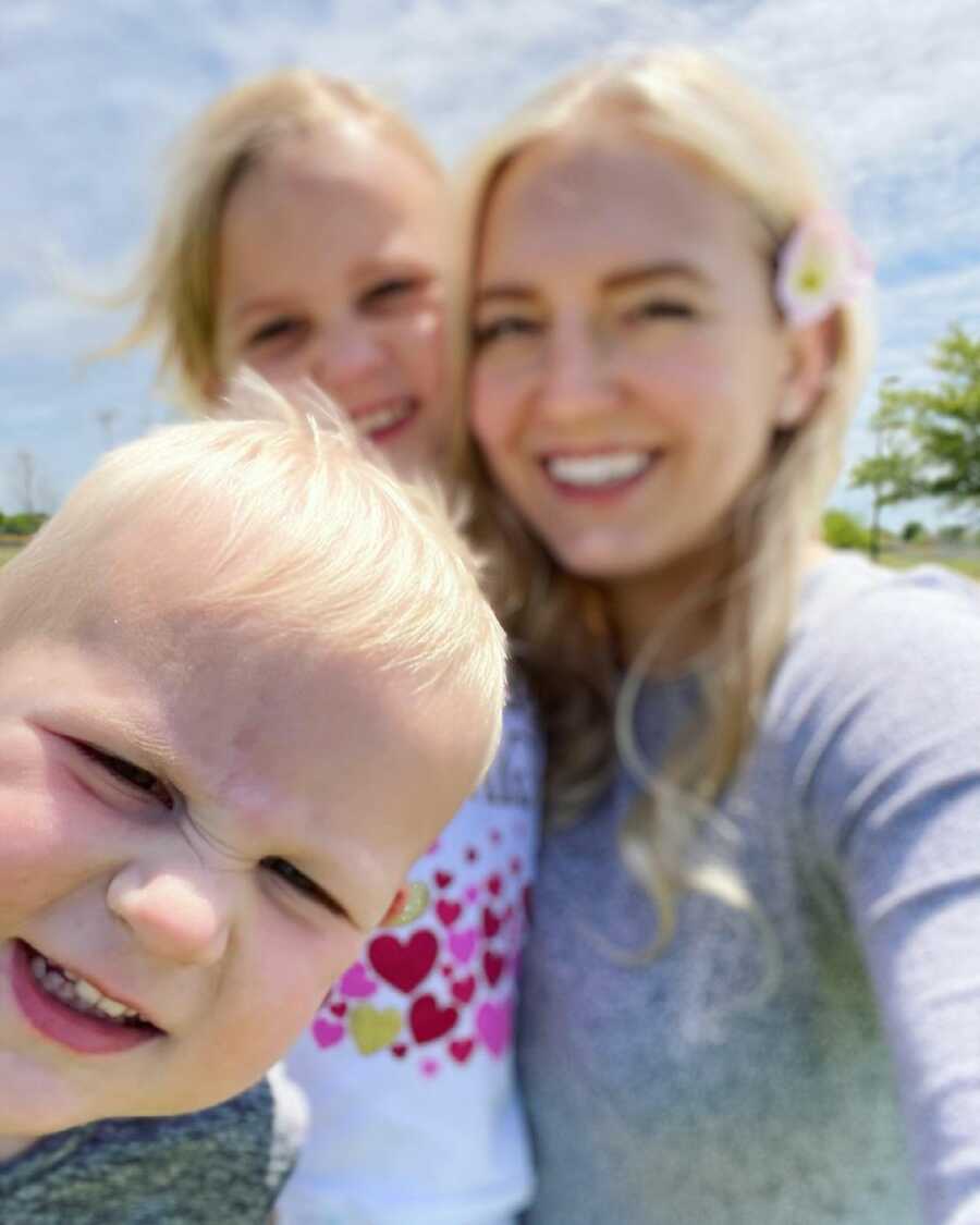 mother takes a selfie with her two kids, son and daughter, the three of them are smiling
