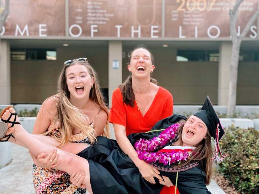 A high school graduate is held by her two sisters