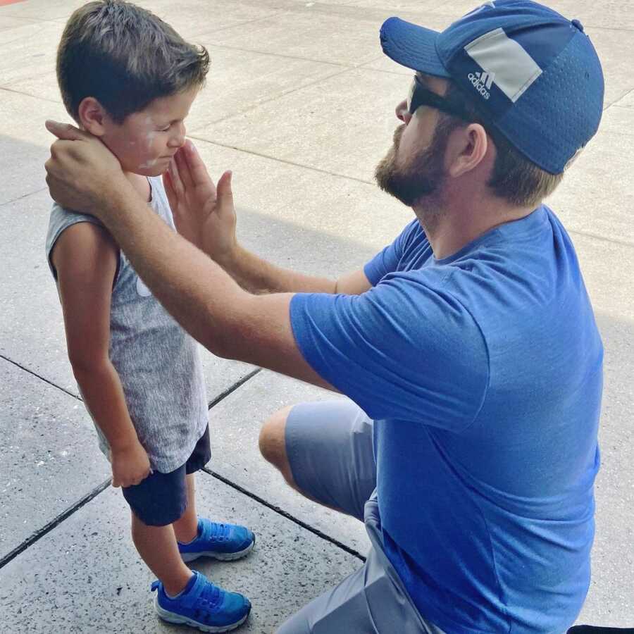 Dad lovingly applies sunscreen to son's face. 