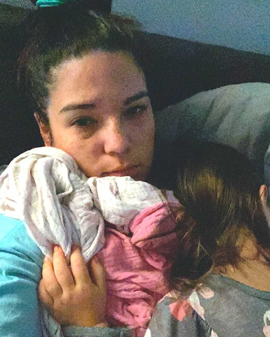 tired looking mother lays with her daughter on her chest while the girl is sleeping peacefully