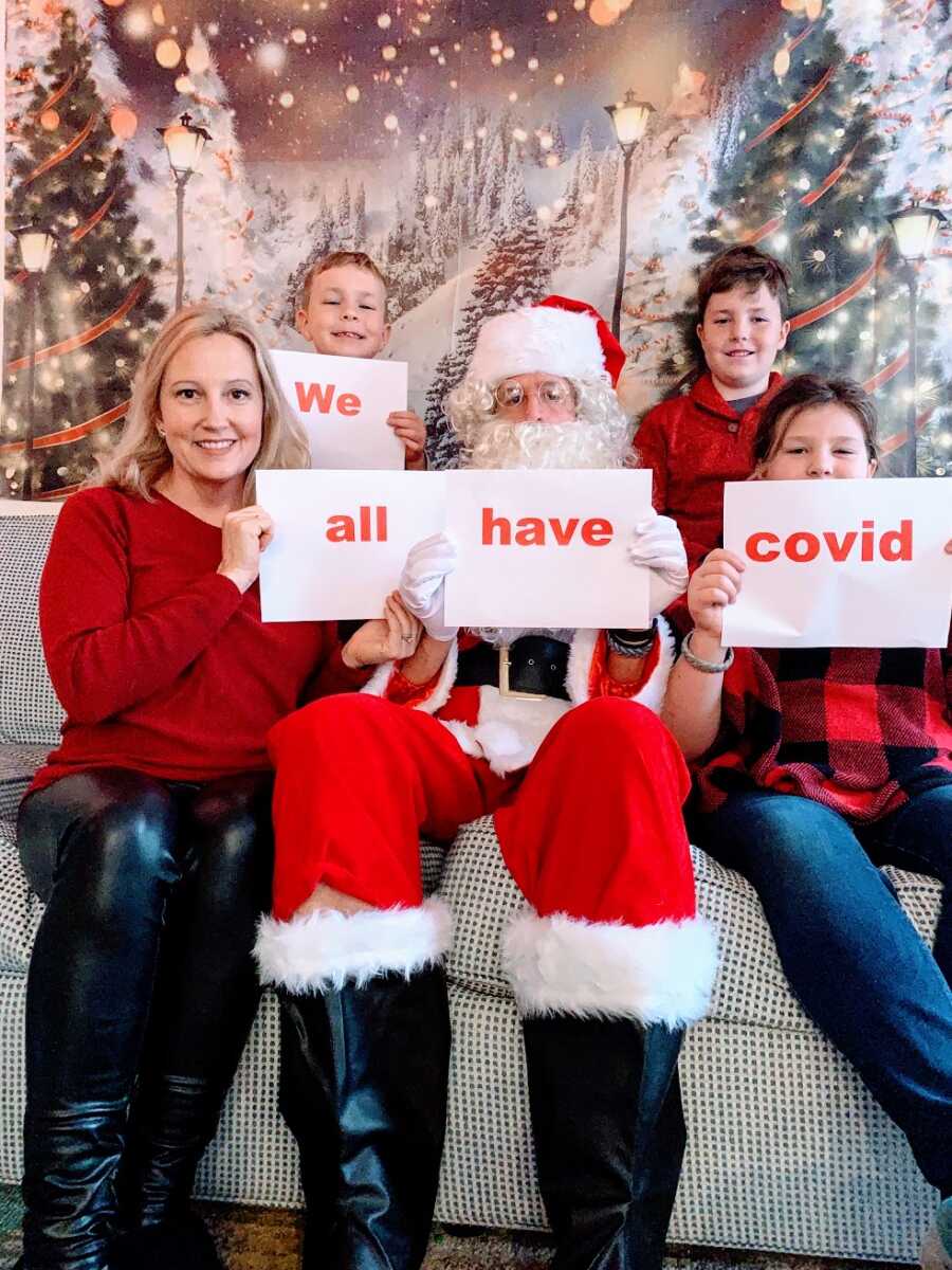 A family sits on the couch with signs saying "We all have Covid"