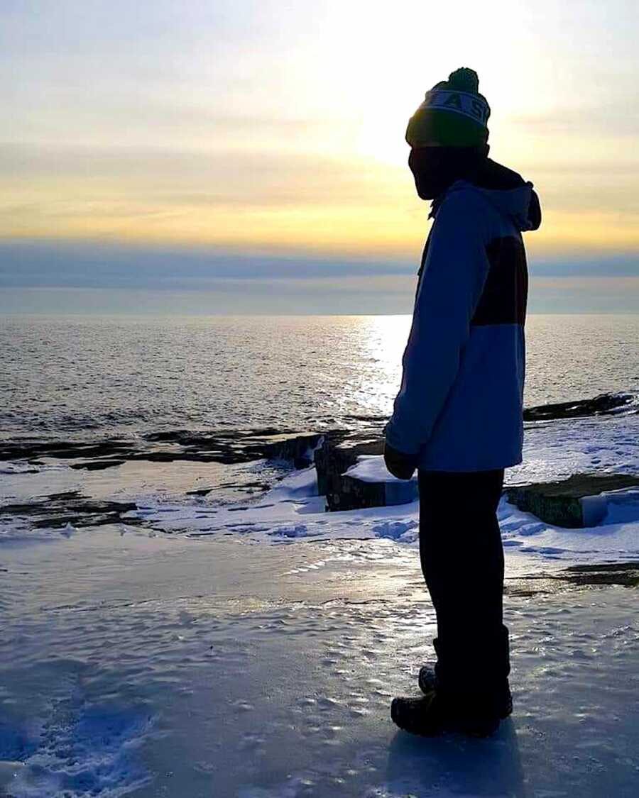 son stands out on ice near the ocean with the sun setting behind him