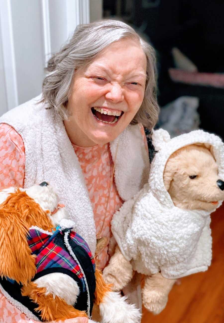 A woman with dementia laughs while holding two stuffed dogs
