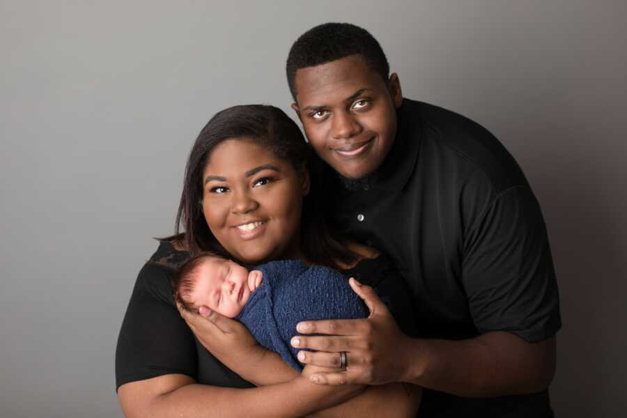 African American couple holds newly adopted white baby boy.
