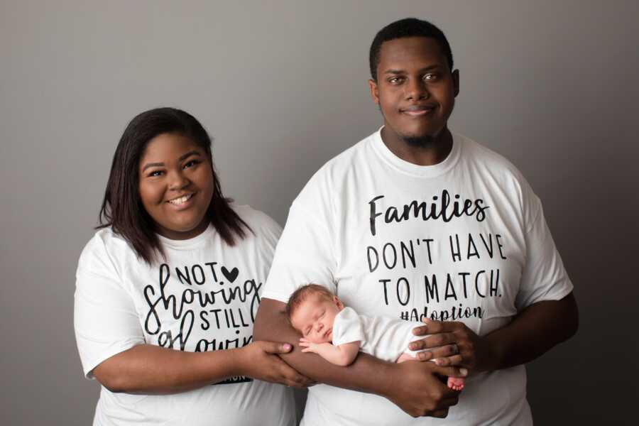 Husband and wife wear adoption shirts and hold their new baby boy.