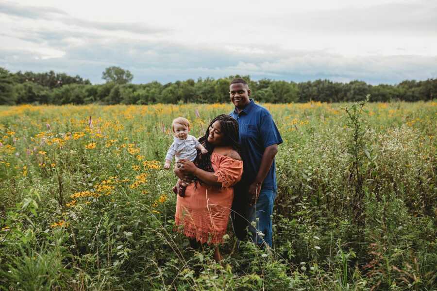 Black couple takes pictures with their adopted son in a field of wildflowers.
