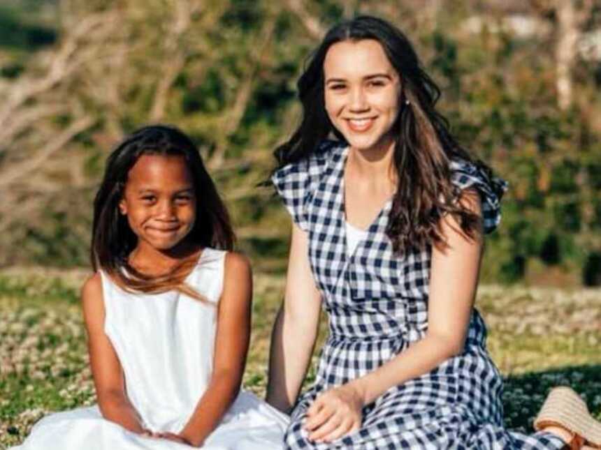 Young mom and daughter in matching dress sitting on picnic blanket