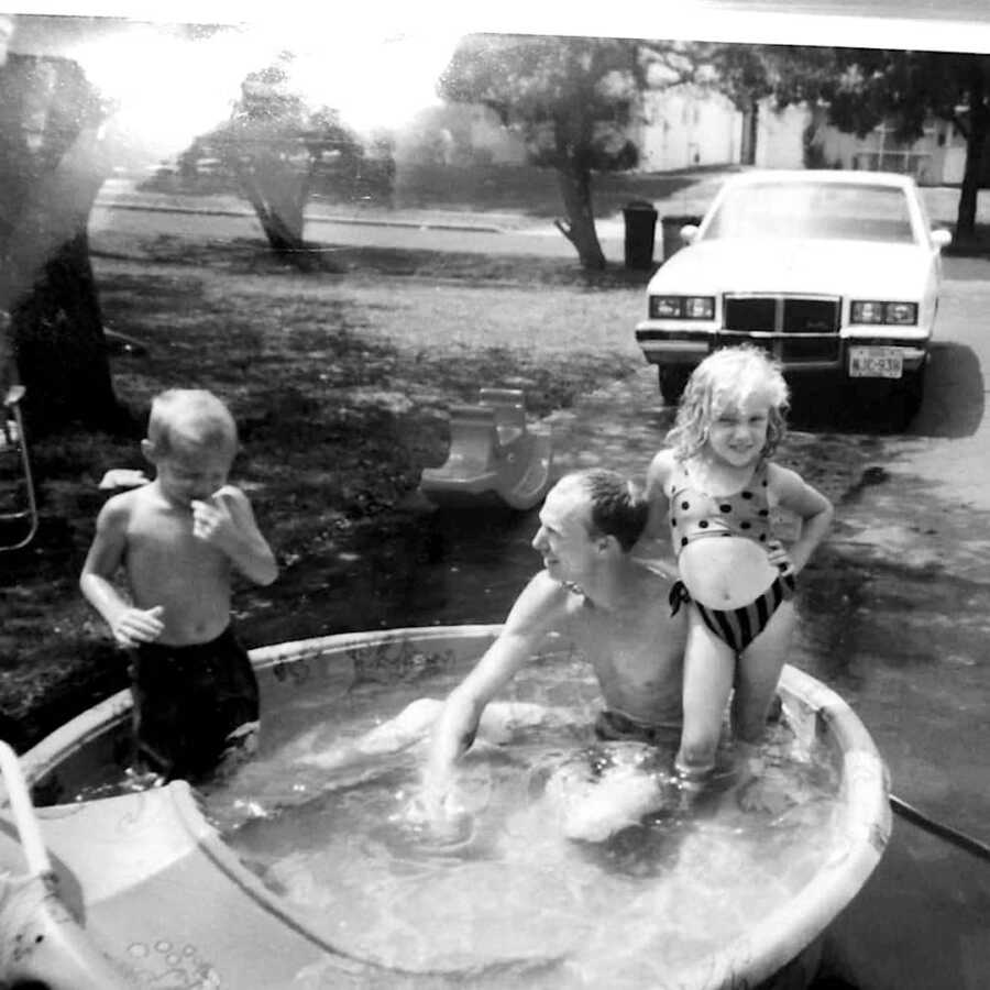 father with his children in a kiddie pool holding onto his daughter and looking towards his son